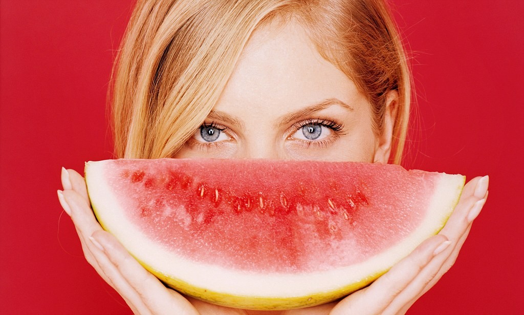 Young woman holding a slice of melon in front of her face --- Image by © Holger Scheibe/Corbis